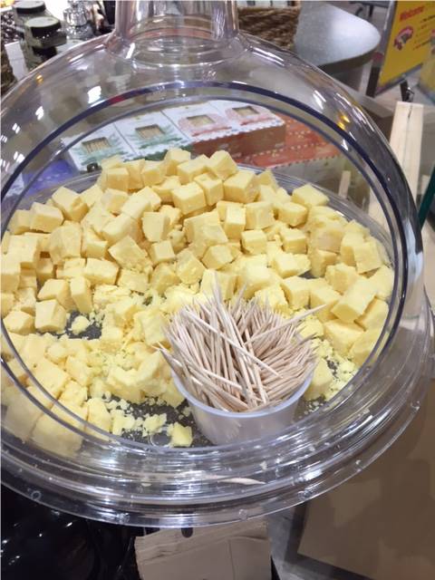 A large bowl of cheese for customers to try with a small container of toothpicks resting inside.
